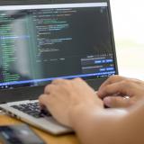 person typing on laptop with colorful computer code visible on the screen