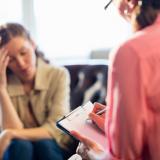woman in chair records answers from despondent women on couch