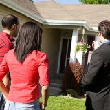 real estate agent and a couple stand in front of a home for a showing