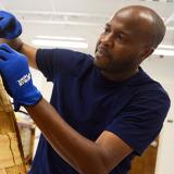 student uses pliers to pull staples and cloth backing off a chair frame