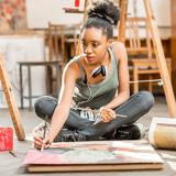 female student sitting on floor painting a still life