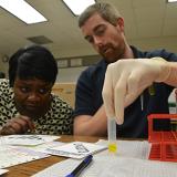 one student holding tube and another student leaning over looking closely at it