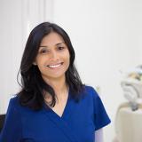person in scrubs standing in forefront with dental chair in background