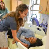 student leaning over bed to help other student lift themselves up