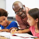smiling teacher assisting elementary student with an assignment