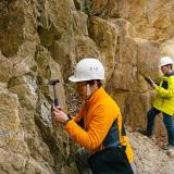 geologist chipping and examining rocks from a cliff face