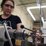 female student watches a grinder carve a metal piece