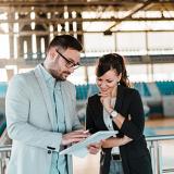 Two individuals wearing professional attire look at a report with gymnasium in background