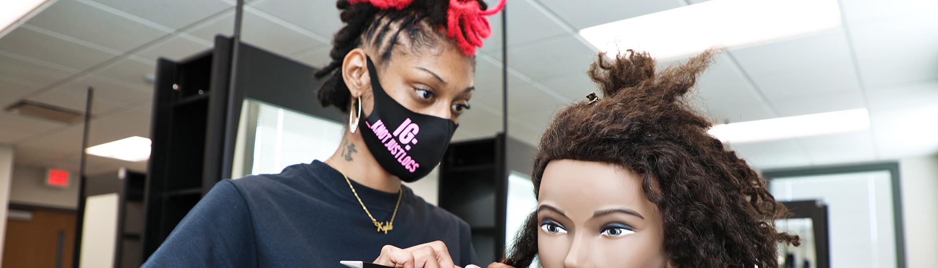Student wearing a mask practices hair care on a dummy head
