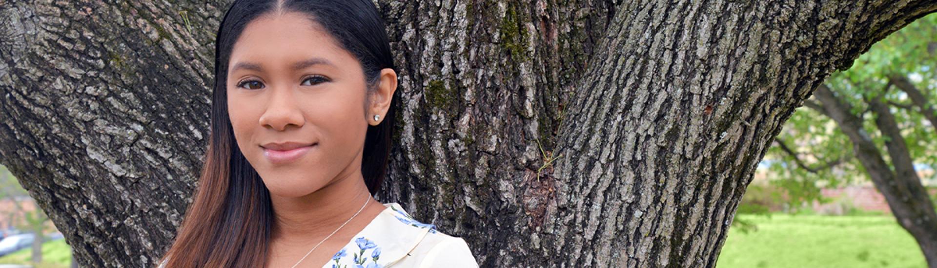 Student smiling in front of tree on main campus. 