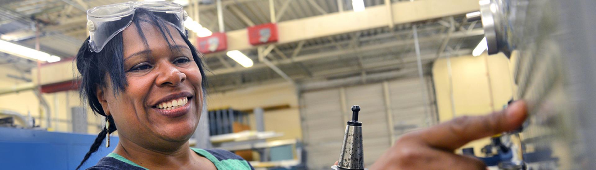 Student wearing safety goggles and pushing button on machining equipment. 
