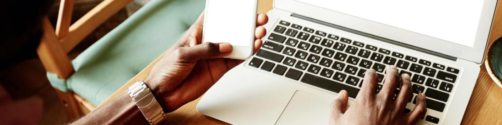 person typing on laptop computer while holding a cell phone
